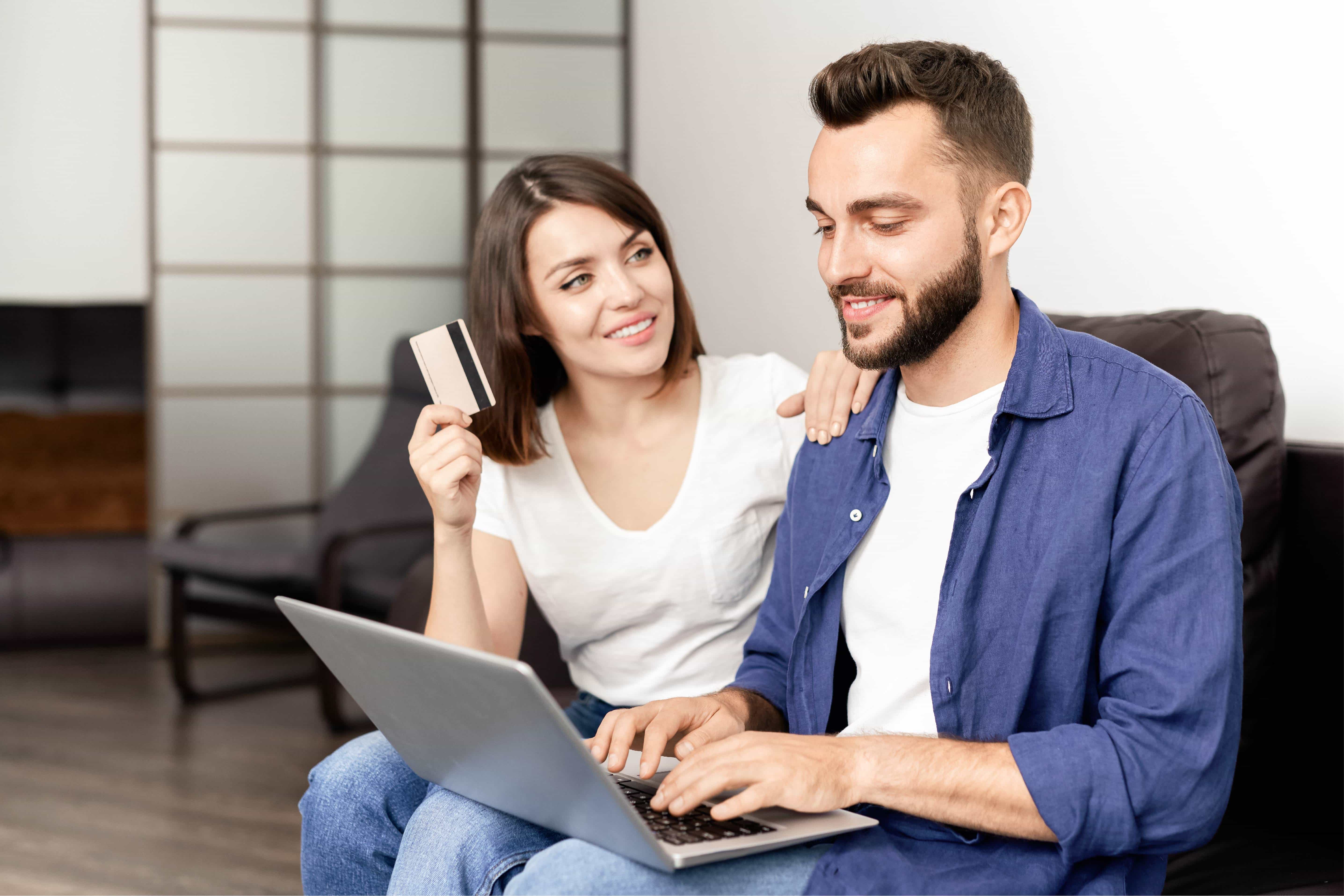 A woman holding a credit card and smiling. She has her arm on a man next to her.