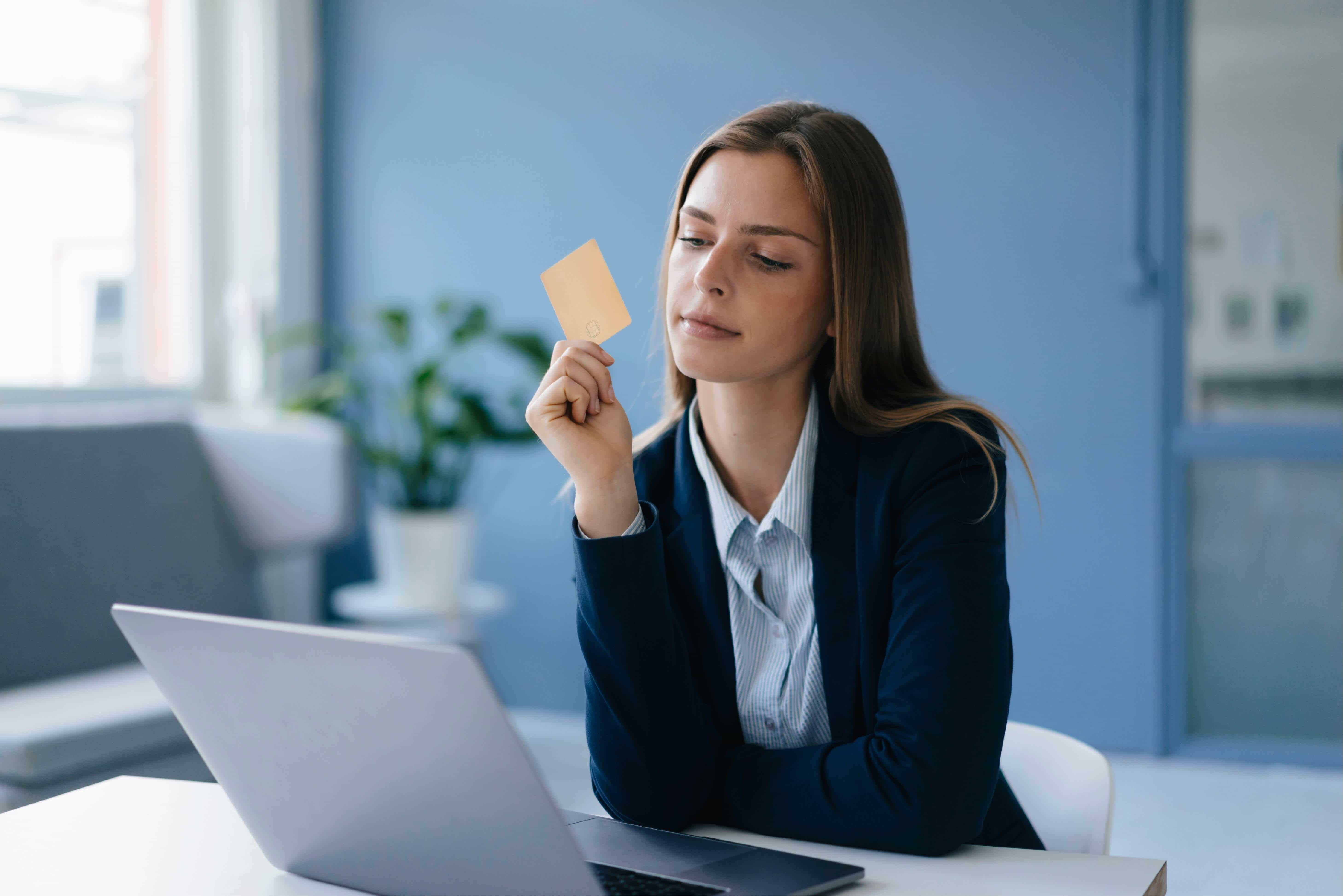 Young business woman conducting an online transaction. She is holding a credit card and has her laptop open in front of her.